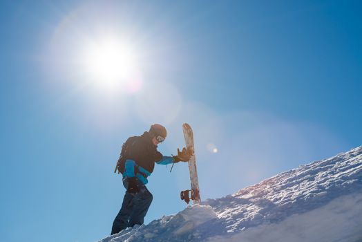 Snowboarder Climbing up with Red Snowboard in the Mountains at Sunny Day. Snowboarding and Winter Sports