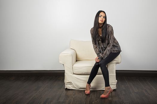 Stylish millenial woman sitting on the arm of white couch
