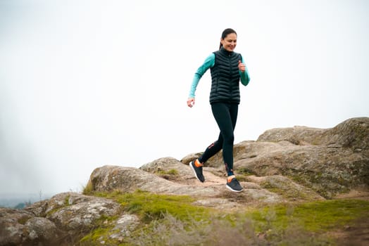 Beautiful Smiling Woman Running on the Mountain Trail at Cold Autumn Evening. Sport and Active Lifestyle Concept.