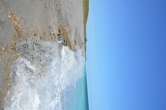 blue ocean water splashing on dirty rocks on the beach