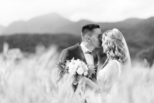 Groom hugging bride tenderly and kisses her on forehead in wheat field somewhere in Slovenian countryside.