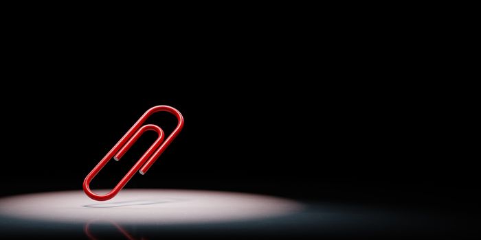 One Red Paperclip Spotlighted on Black Background