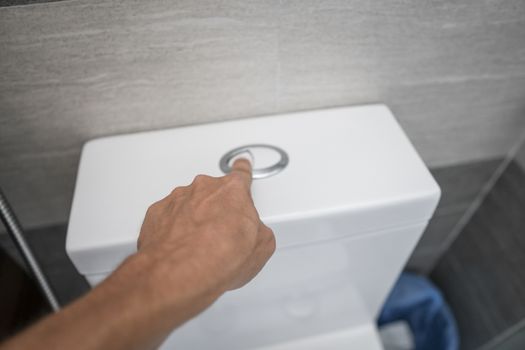 Close up of finger pushing a flush toilet button for cleaning a toilet.