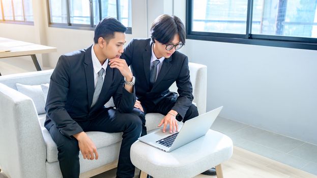 A group of 2 male business men are working with computers seriously in the office.