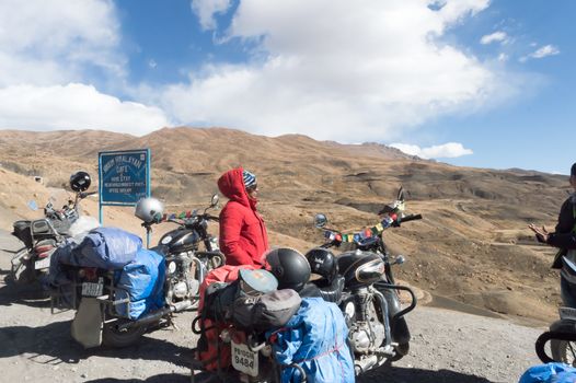 Indian woman traveler trekker and Biker standing beside her motorcycle, hiking high Himalayan Mountain region outing and exploring local hill station. Adventure Tourism. Kaza India Asia October 2019
