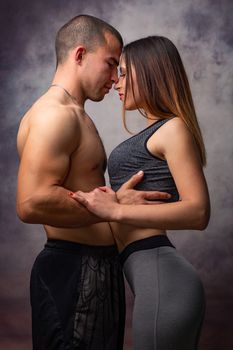 Young loving couple of athletic physique cuddles on grey background