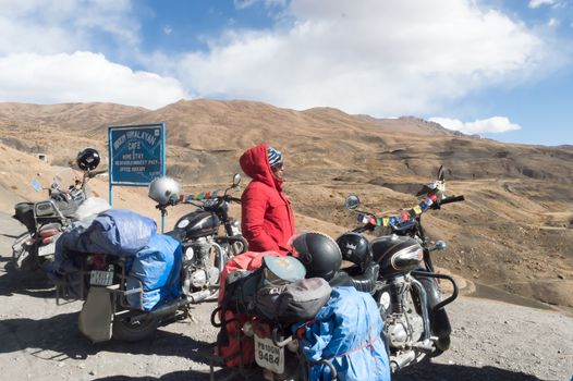 Indian woman traveler trekker and Biker standing beside her motorcycle, hiking high Himalayan Mountain region outing and exploring local hill station. Adventure Tourism Team. Kaza India October 2019