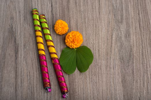 Indian Festival Dussehra and Navratri, showing golden leaf (Bauhinia racemosa) and marigold flowers with Dandiya sticks on a wooden background