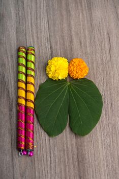 Indian Festival Dussehra and Navratri, showing golden leaf (Bauhinia racemosa) and marigold flowers with Dandiya sticks on a wooden background
