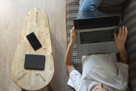 Woman with a laptop laying on a sofa. Study and work online, freelance. Self employed woman, girl working with her notebook laying on a couch with a phone, smartphone and ereader on table.
