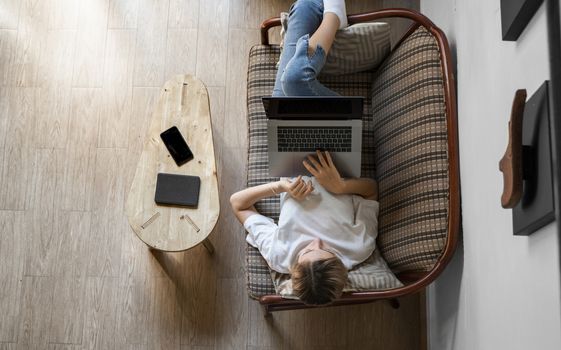 Woman with a laptop laying on a sofa. Study and work online, freelance. Self employed woman, girl working with her notebook laying on a couch with a phone, smartphone and ereader on table.