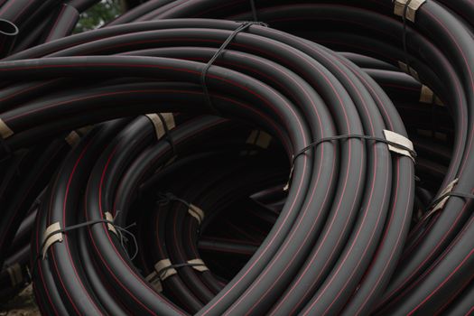 Black rubber or plastic pipes with a red lines as a construction material and equipment at building site. Using as a water pipe.