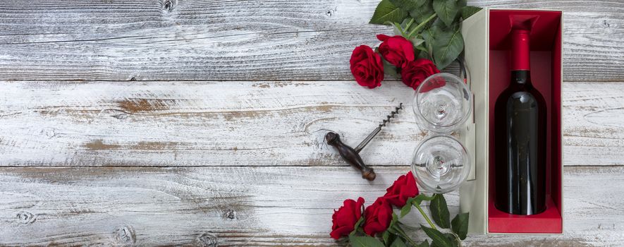 Happy Valentines Day celebration with red roses and a bottle of wine on white rustic wooden background with copy space available   