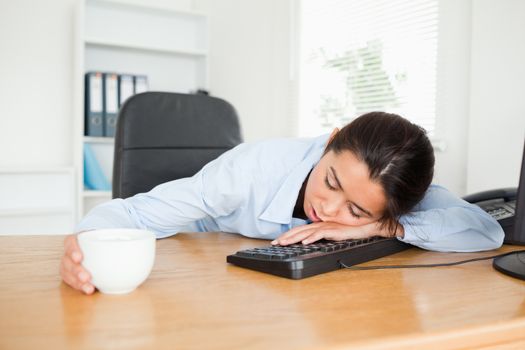 Frontal view of a pretty woman sleeping on a keyboard while holding a cup of coffee