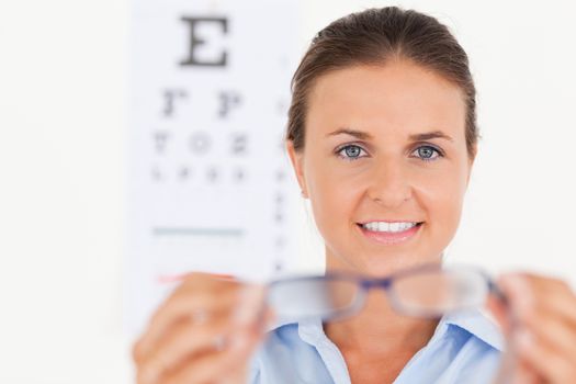 Portrait of a brunette eye specialist handing out glasses looking into the camera