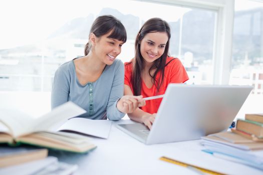 Two girls smiling as they use the laptop as one girl points at something 