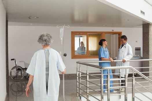 Old woman walking along the hallway in a hospital with a drip in her hand