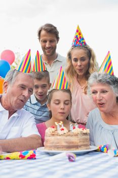 Cheeful family watching girl blowing out candles at birthday party
