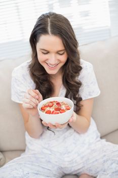 Cheerful pretty woman in pyjamas eating fruity cereal