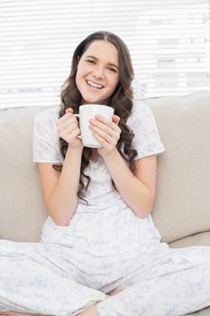 Smiling young woman in pyjamas having coffee