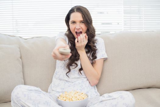 Pretty woman in pyjamas having popcorn while watching scary movie