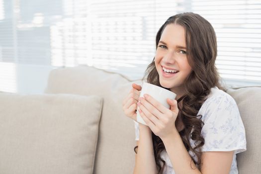 Cheerful young woman in pyjamas having coffee