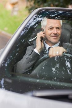 Smiling businessman on the phone driving expensive cabriolet