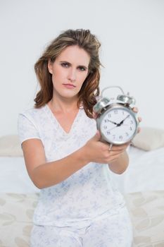 Frowning tired woman showing alarm clock