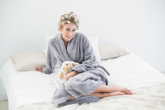 Pleased relaxed blonde woman in hair curlers cuddling a plush sheep