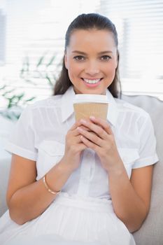 Smiling pretty woman having coffee sitting on cosy couch