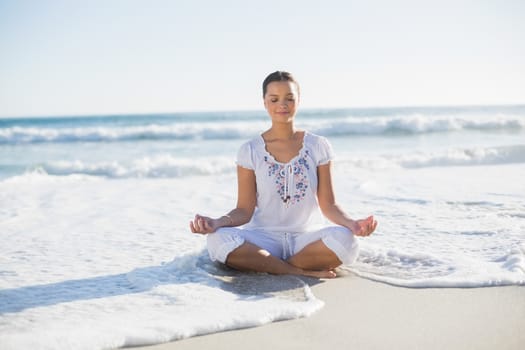 Peaceful pretty woman in lotus position on the beach with wave reaching her