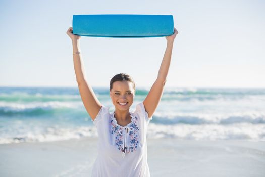 Smiling woman holding exercise mat over her head