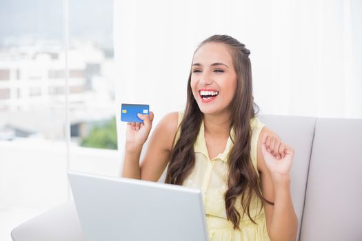 Victorious young brunette holding credit card