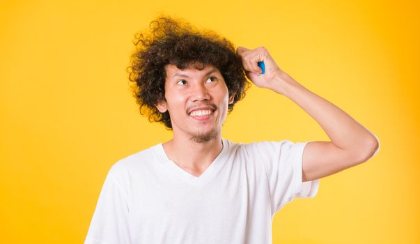Asian man combing curly hair on yellow background