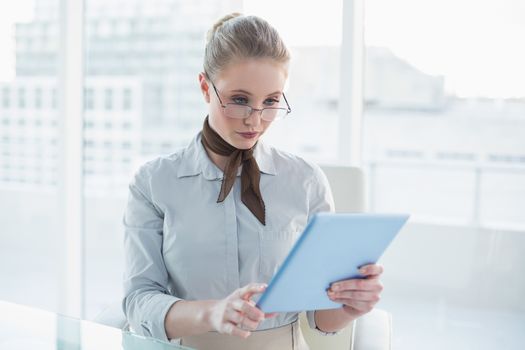 Blonde stern businesswoman looking at tablet