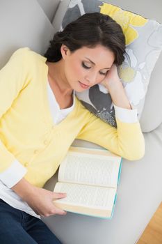 Calm casual brunette in yellow cardigan reading a book