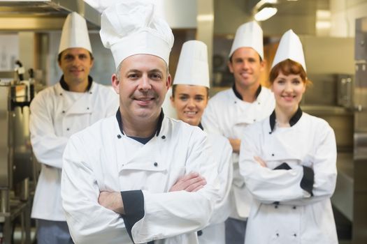 Five chefs wearing uniforms posing in a kitchen