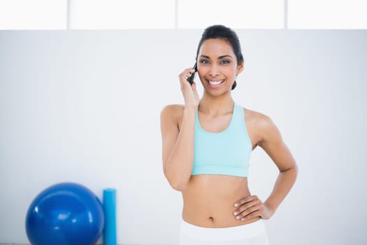 Gleeful sporty woman phoning while standing in fitness hall