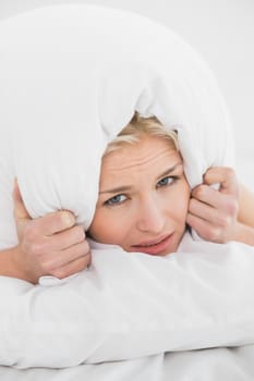 Displeased woman covering ears with pillow in bed