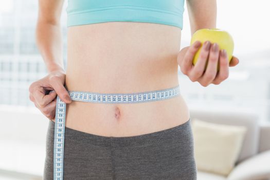 Mid section of woman measuring waist with apple in hand