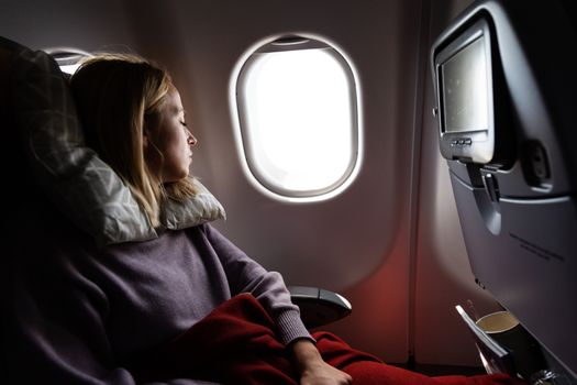 Tired blonde casual caucasian woman sleeping on seat while traveling by airplane on long distance transatlantic flight. Commercial transportation by planes.