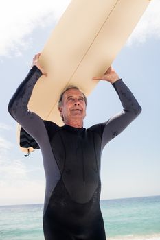 Senior man in wetsuit running with surfboard over his head