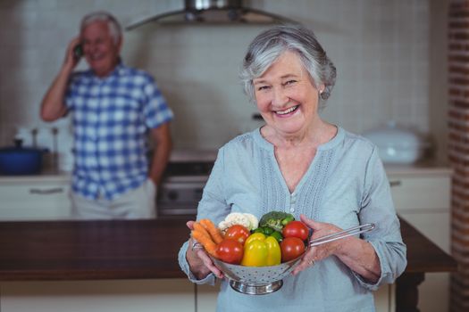 Senior woman holding colander with vegetables