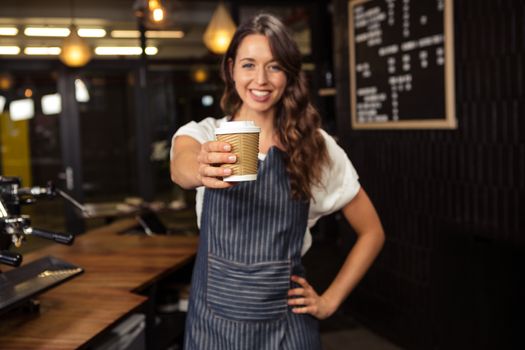 Smiling barista holding disposable cup