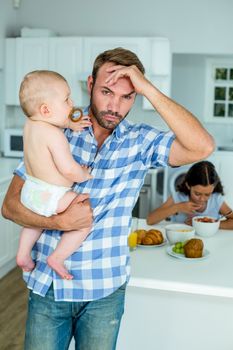 Worried mid adult man holding baby in kitchen