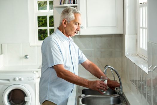 Calm senior man filling water in glass while standing at sink