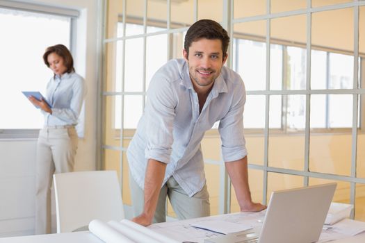Businessman working on blueprints with colleague in background at office