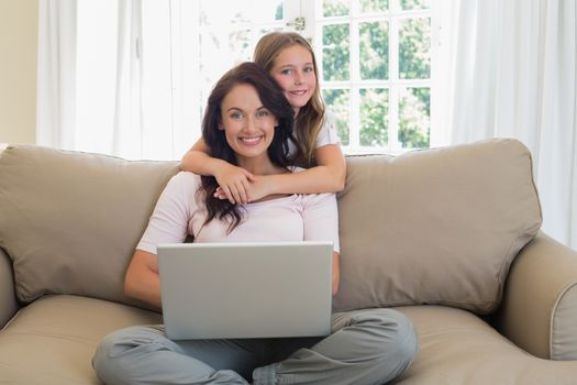 Girl embracing mother using laptop on sofa