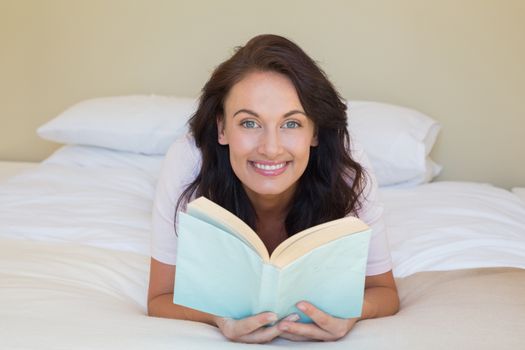 Woman holding book while lying in bed