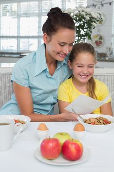 Mother and daughter reading greeting card at breakfast table